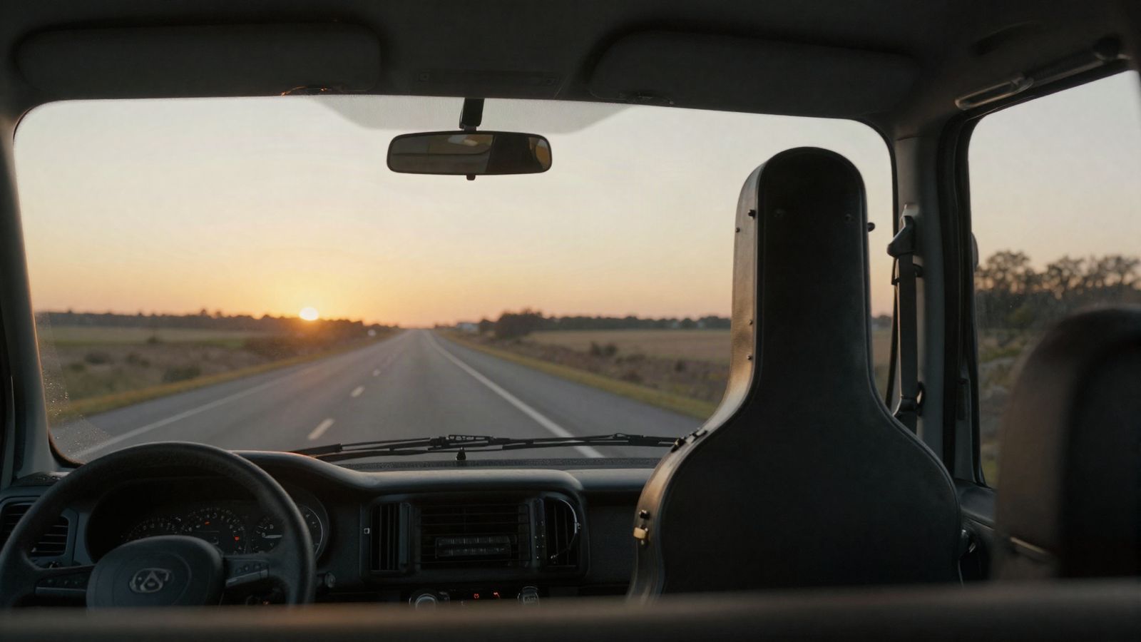 An open highway at sunrise, seen through a van windshield with a guitar case on the seat
